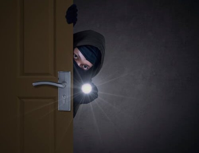 burglar peeping around a door and shining a flashlight