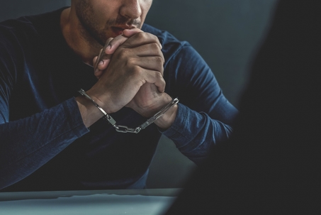 Criminal man with handcuffs in interrogation room being interviewed