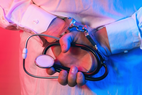doctor in handcuffs holding stethoscope