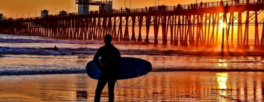 man holding surfboard on beach at sunset