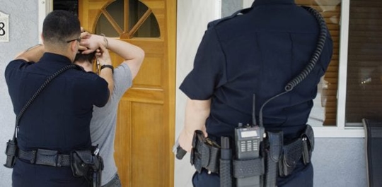 two police officers detaining a client and hold his hands over his head